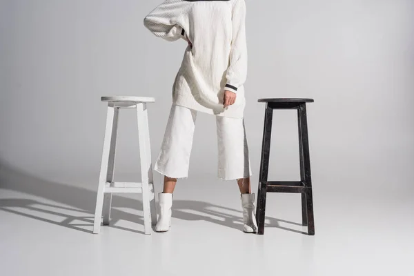 Cropped image of girl in stylish white clothes standing between black and white chairs on white — Stock Image Cropped Image Girl Stylish White Clothes Standing Black White Chairs Stock Image