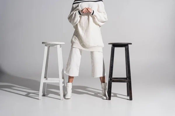 Cropped image of girl in stylish sweater and trousers standing between black and white chairs on white — Stock Image Cropped Image Girl Stylish Sweater Trousers Standing Black White Chairs Stock Picture