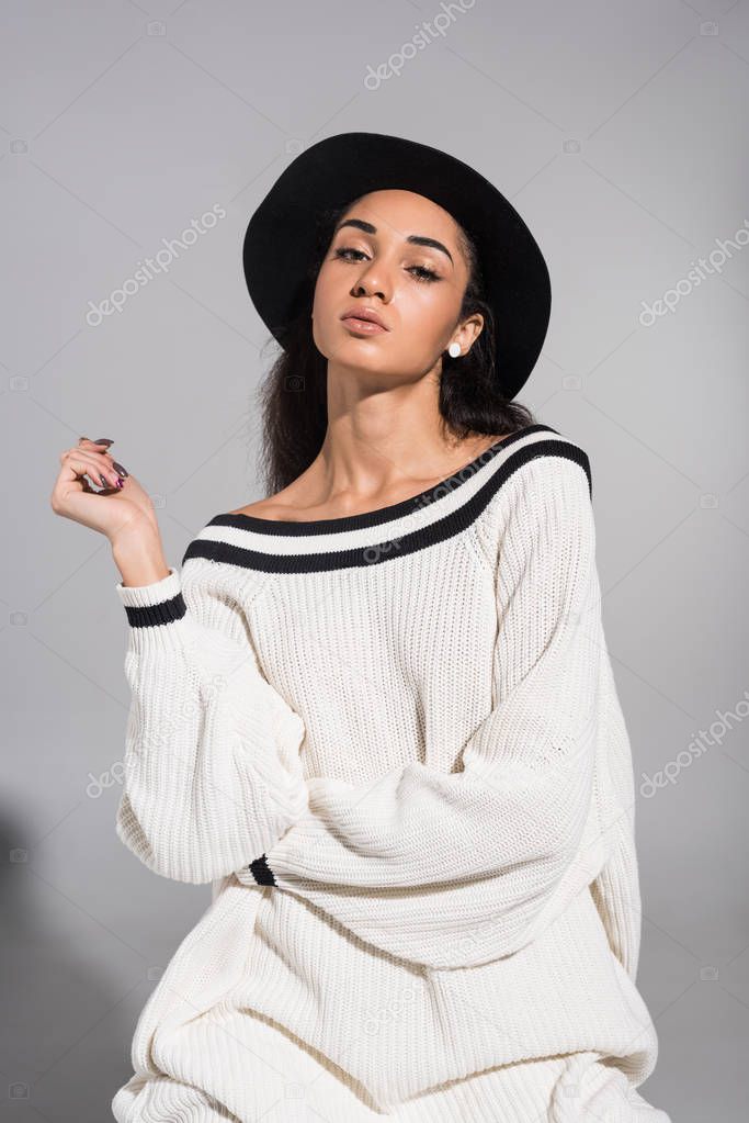 attractive african american young woman in stylish white clothes and hat looking at camera on white