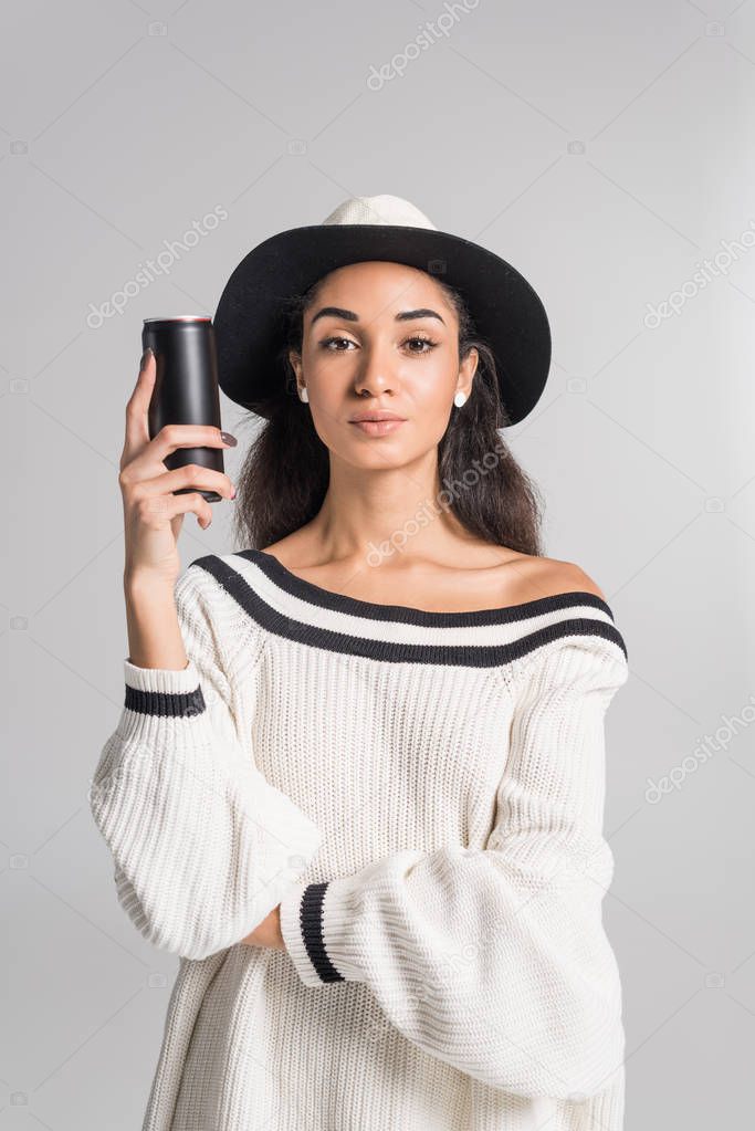 attractive african american girl in stylish white sweater and hat holding black can isolated on white