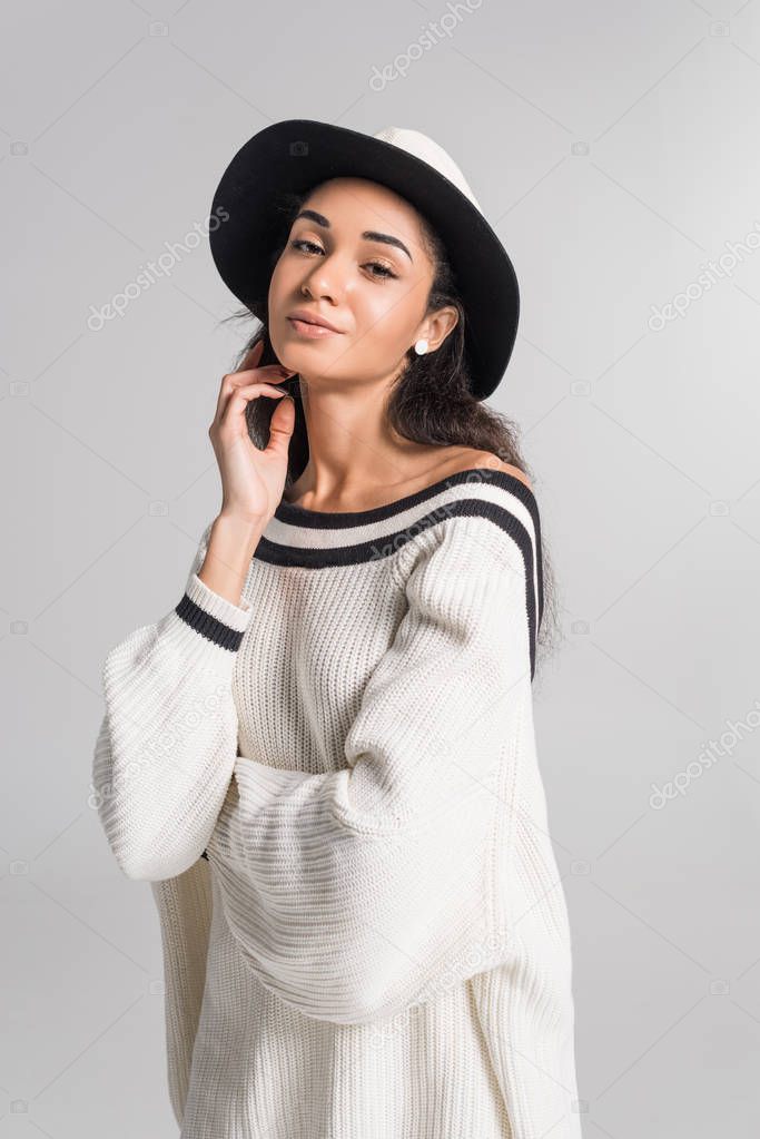 beautiful cheerful african american girl in stylish white sweater and hat posing isolated on white