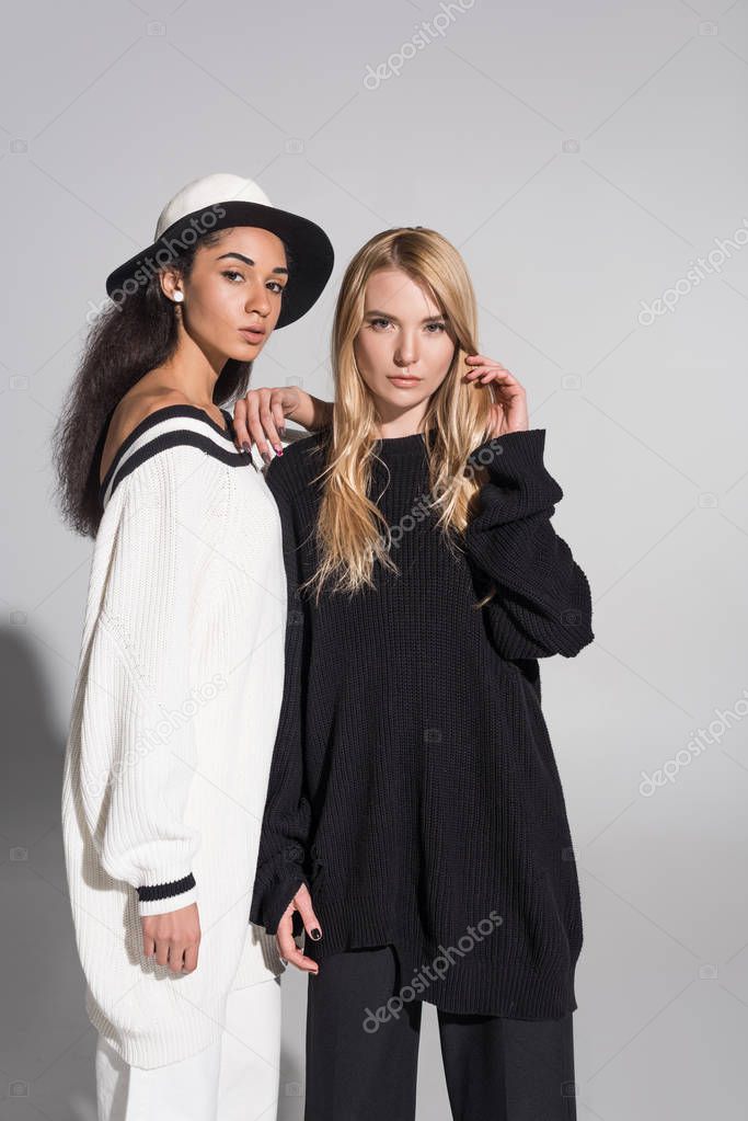 attractive multicultural female models in black and white clothes standing and looking at camera on white