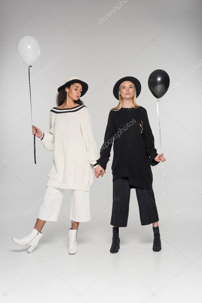 beautiful multiethnic lesbian couple in black and white clothes holding hands and two balloons on white