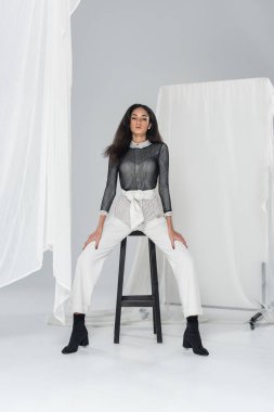 Beyaz tül yakın sandalyede oturan şık giysiler içinde çekici Afrikalı-Amerikalı kadın