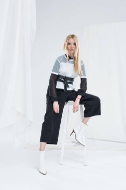 güzel beyaz sarışın kadını sandalyede oturan ve üzerinde beyaz izole kamera seyir siyah giyimleri