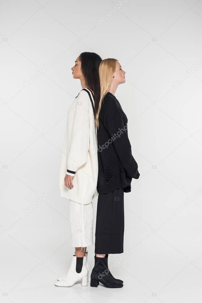 beautiful multicultural women in black and white clothes standing back to back on white