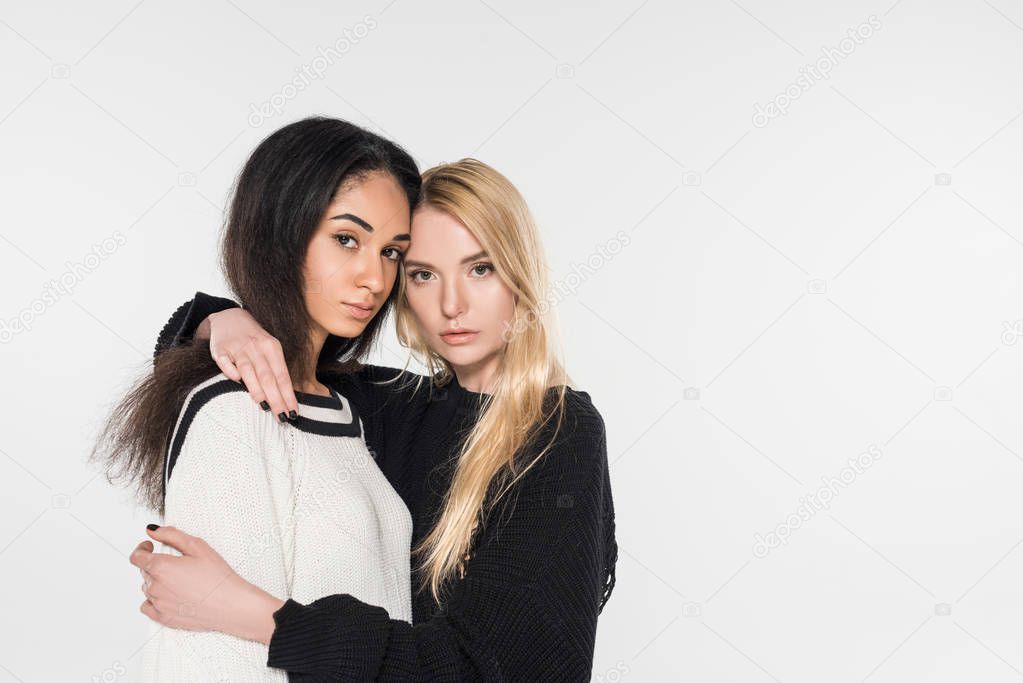 beautiful multicultural lesbian couple in black and white clothes hugging and looking at camera isolated on white
