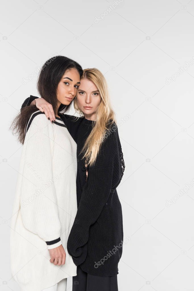 attractive multiethnic lesbian couple in black and white clothes hugging and looking at camera isolated on white