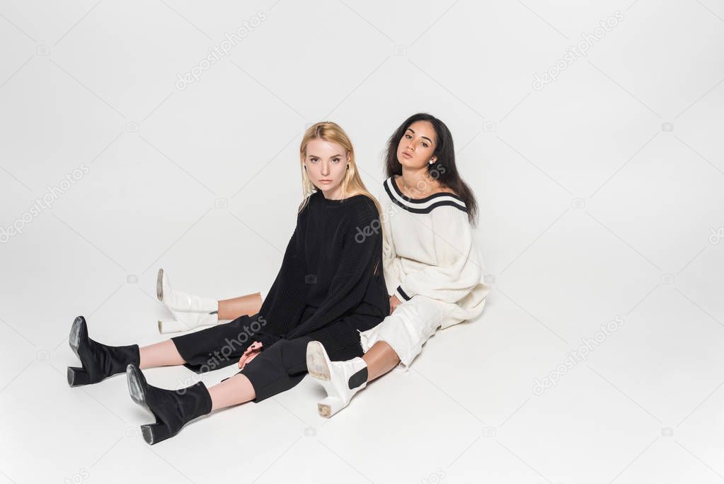 beautiful multicultural women in black and white clothes sitting and looking at camera on white