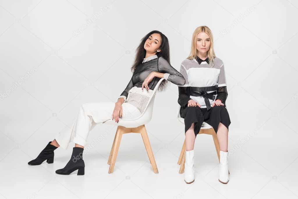 caucasian and african american women in black and white clothes sitting on chairs isolated on white