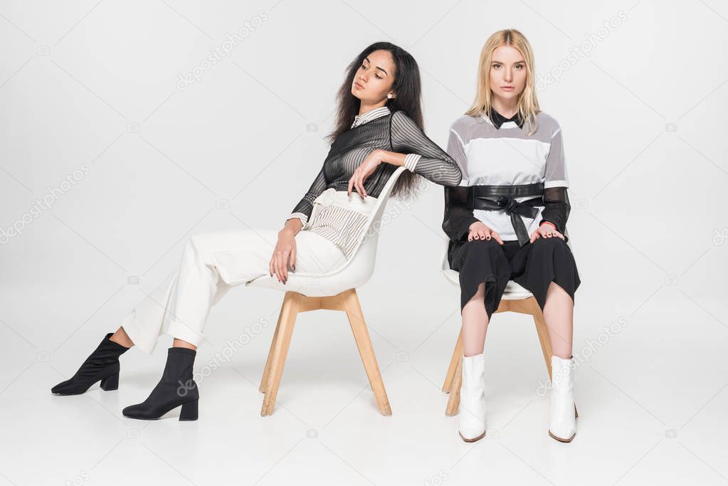 african american and caucasian women in black and white clothes sitting on chairs isolated on white