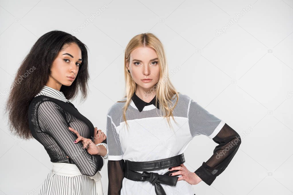 confident attractive multiethnic women in black and white clothes looking at camera isolated on white