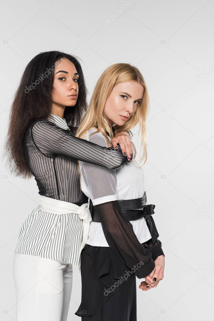 attractive african american woman hugging caucasian girlfriend in black and white clothes hugging isolated on white, looking at camera