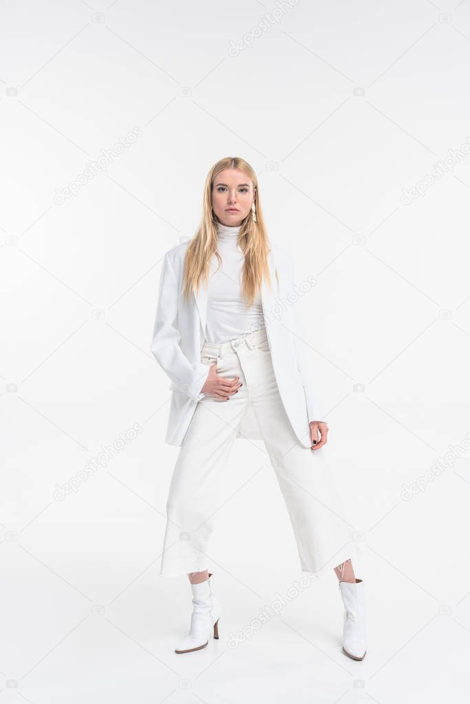 attractive caucasian blonde woman in fashionable white clothes posing and looking at camera isolated on white