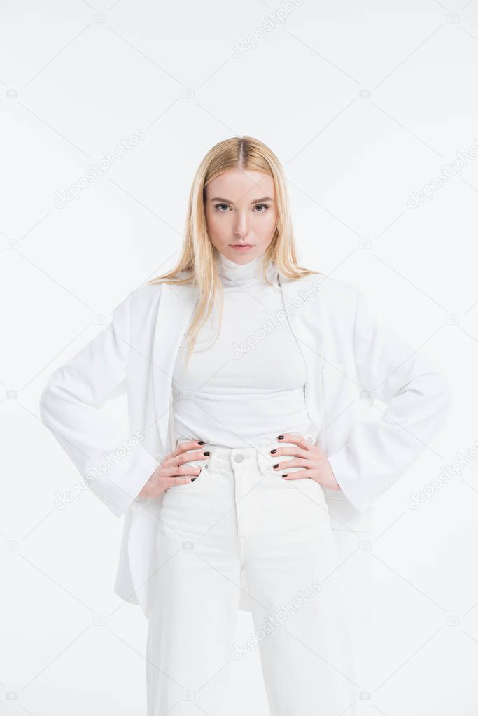 attractive caucasian blonde woman in fashionable white clothes posing with hands akimbo isolated on white