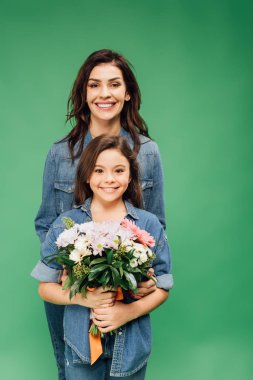 Anne ve kızı kameraya bakarak ve yeşil izole çiçek buketi holding