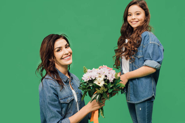 счастливая мать и дочь с цветами глядя на камеру изолированы на зеленый
