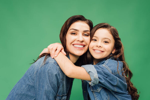 счастливая мать и дочь обнимаются и смотрят на камеру, изолированную на зеленый
