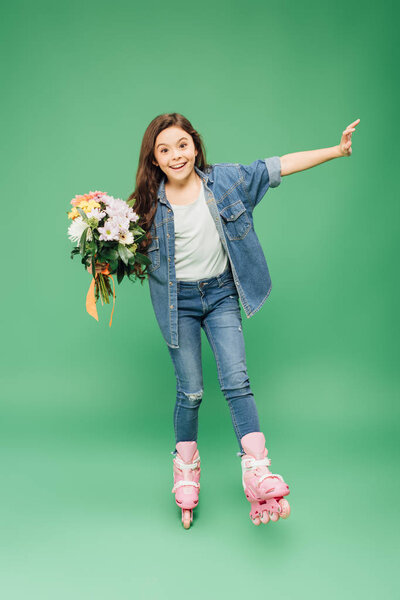 excited child in rollerblades with flower bouquet on green background