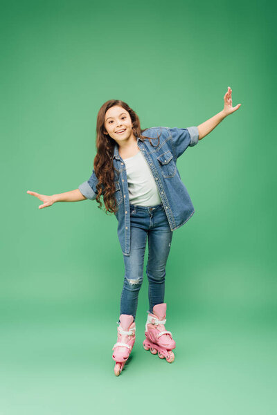 happy child rollerblading with outstretched hands on green background
