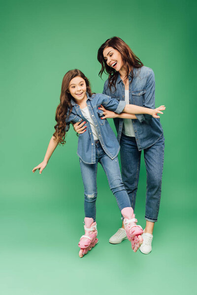 smiling mother teaching daughter rollerblading on green background