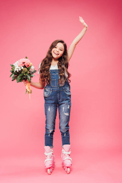 adorable smiling child in roller blades with flower bouquet raising hand on pink background