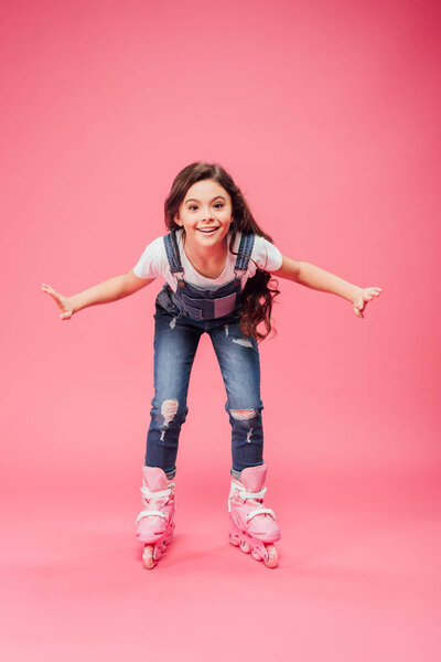 happy child in overalls rollerblading on pink background