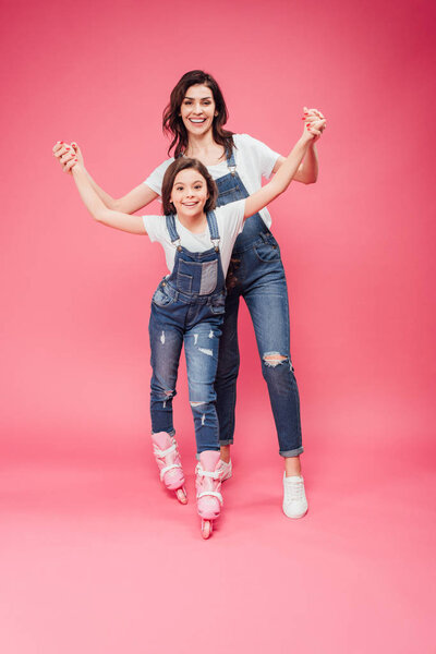 beautiful mother teaching daughter rollerblading on pink background