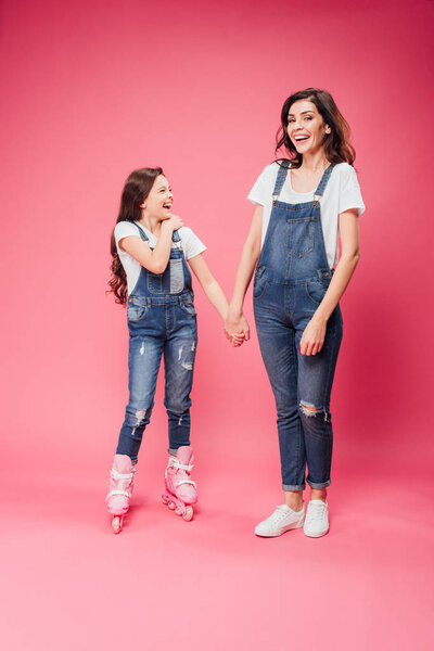 daughter in roller blades holding hands with happy mother on pink background