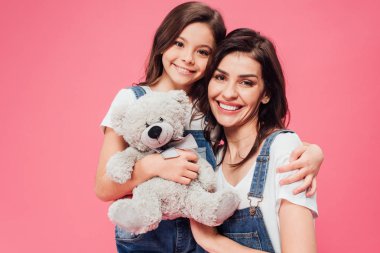 gülümseyen kızı anne ve holding yumuşak oyuncak pembe üzerinde izole sarılma 
