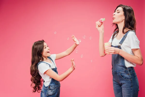 Mãe Soprando Bolhas Sabão Perto Filha Alegre Isolada Rosa — Fotografia de Stock