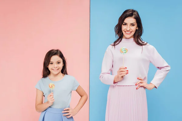 可爱的孩子和有吸引力的女人拿着糖果 看着相机在蓝色和粉红色的背景 — 图库照片