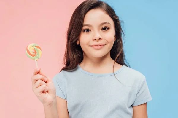 青色とピンク色の背景にカメラを見ながらお菓子を保持している愛らしい子 — ストック写真