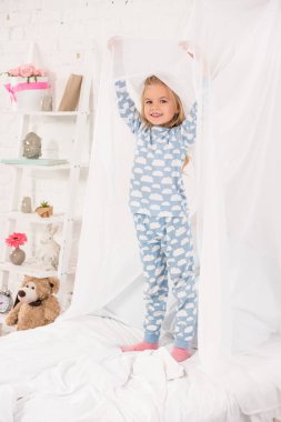 smiling kid in pajamas standing on bed and touching canopy clipart