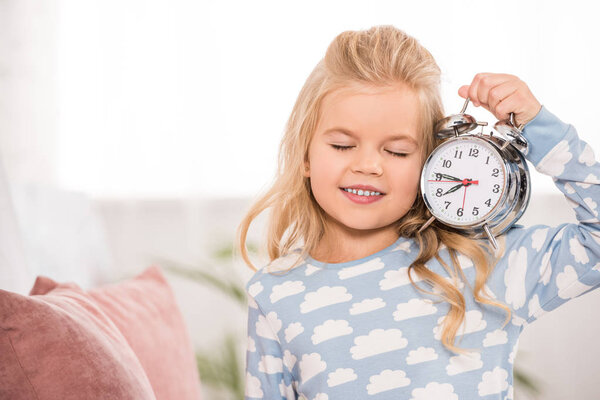 smiling adorable child with clock and closed eyes in bedroom 