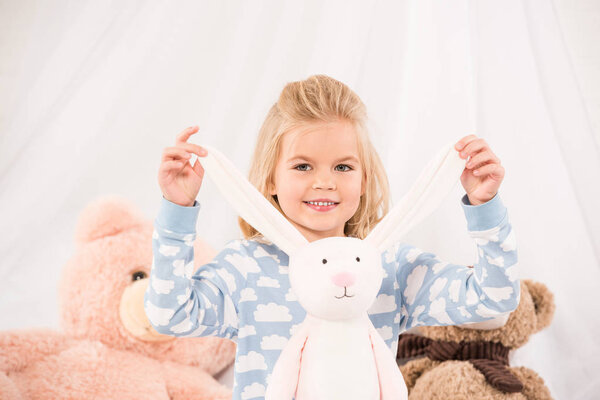 улыбающийся очаровательный ребенок играет с мягкими игрушками в спальне
