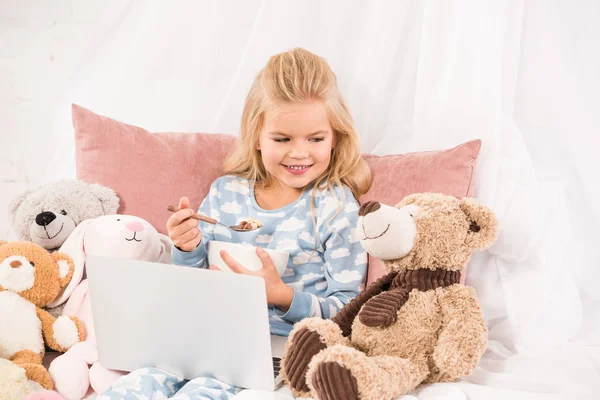 Cute Child Laptop Eating Cornflakes Looking Teddy Bear Bed — Stock Photo, Image