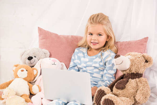 adorable child sitting in bed with soft toys and watching cartoons