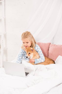 yatakta yatarken, corgi köpek sarılma ve dizüstü evde kullanma çok güzel çocuk
