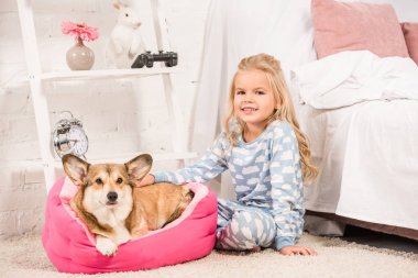 Galce corgi köpek ile oturan ve evde kameraya bakarak pijama şirin çocuk 