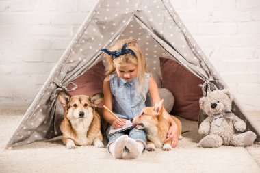 Kızılderili çadırı corgi köpek ve defterde evde yazma ile oturma sevimli çocuk