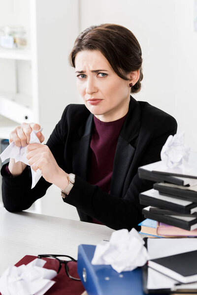 sad attractive businesswoman tearing papers and looking at camera in office