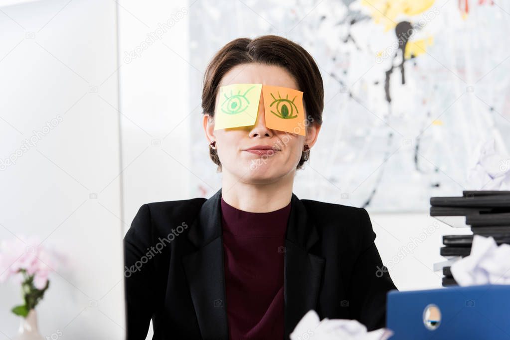 grimacing businesswoman sitting with stickers on eyes in office