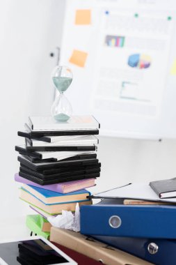 hourglass on stack of DVDs and folders in light business office clipart