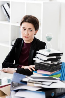attractive sad businesswoman looking at hourglass in office clipart