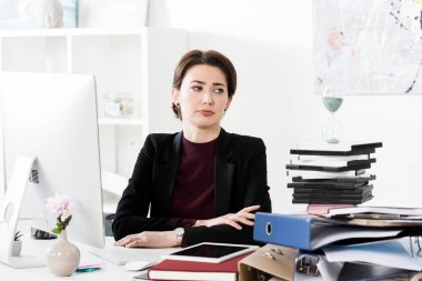 attractive sad businesswoman looking at hourglass at work clipart