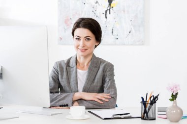bilgisayar Office ile masada oturan ve kameraya bakarak gri takım elbiseli çekici iş kadını