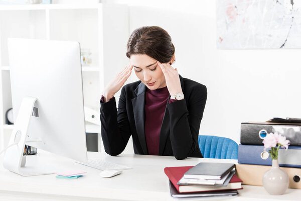 sad exhausted businesswoman having headache and touching head in office