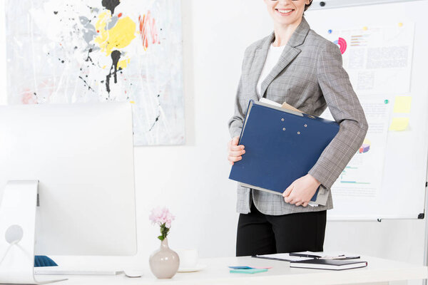 cropped image of smiling businesswoman holding folder with documents in office
