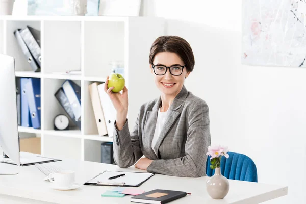 Smilende Attraktiv Forretningskvinne Som Holder Eple Kontoret Ser Kamera – stockfoto